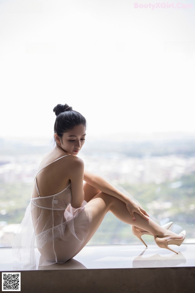 A woman sitting on a window sill in a white lingerie.