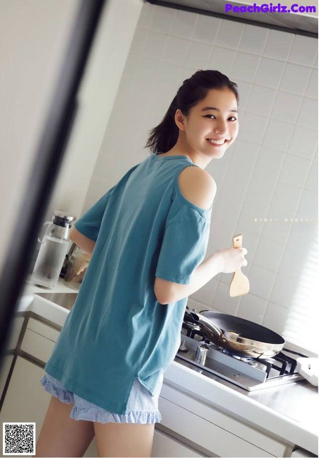 A woman standing in a kitchen holding a wooden spoon.