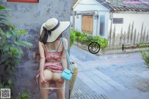 A woman wearing a hat and a face mask leaning against a wall.