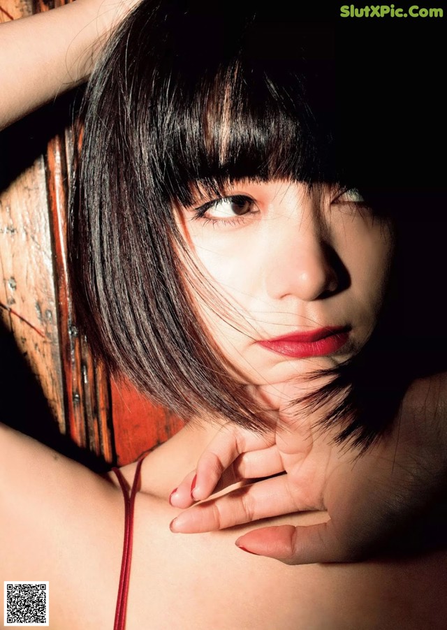 A woman in a red dress leaning against a wooden wall.