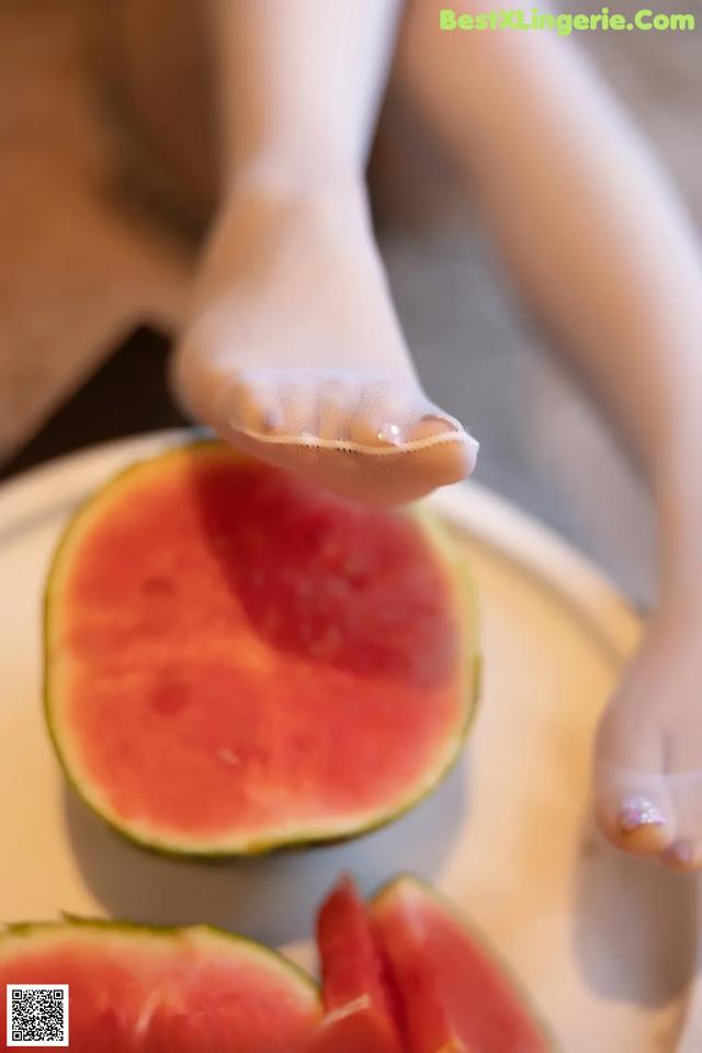 A woman's feet on a plate with a slice of watermelon.