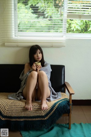 A naked woman leaning against a wall with a towel around her neck.