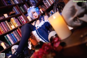 A woman with blue hair sitting on the floor in front of a book shelf.