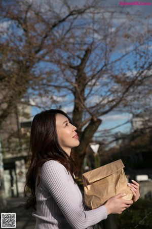 A woman walking down a sidewalk holding a brown bag.