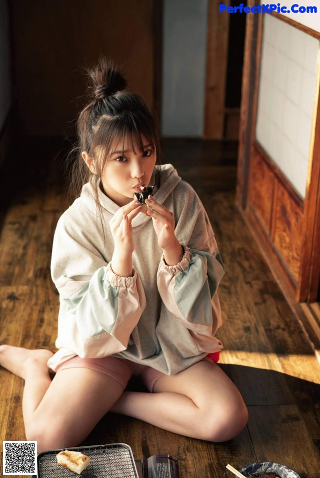 A woman sitting on the floor eating a piece of food.