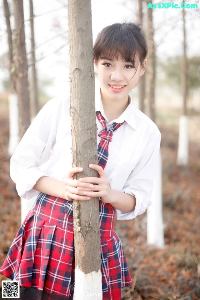 A young woman in a school uniform leaning against a tree.