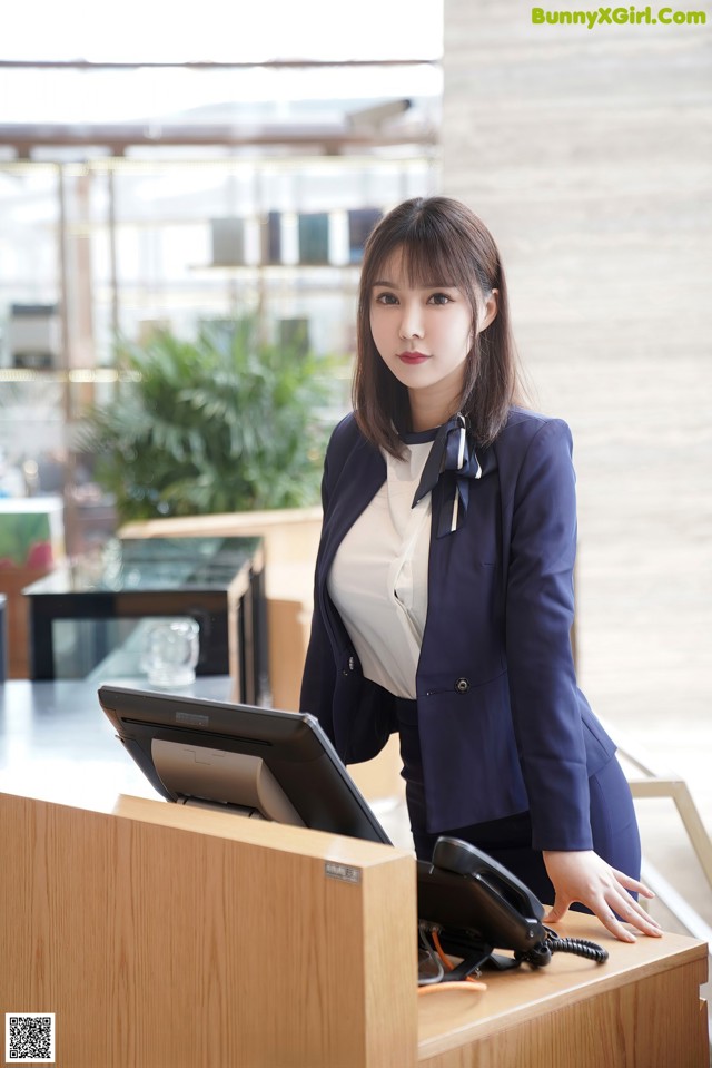 A woman in a business suit standing at a reception desk.