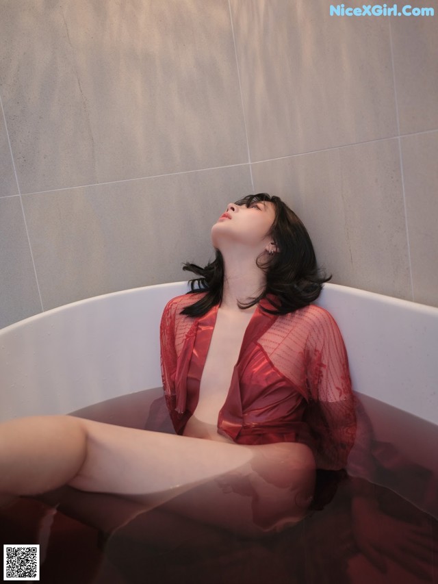 A woman in a red robe sitting in a bathtub.