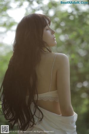 A woman in a white lingerie sitting under a tree.