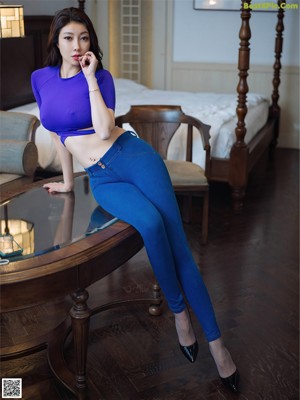 A woman in a purple top and blue jeans sitting on a table.