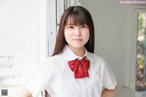 A young woman sitting on a stool wearing a school uniform.