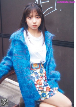 A woman in a blue tank top leaning against a wall.