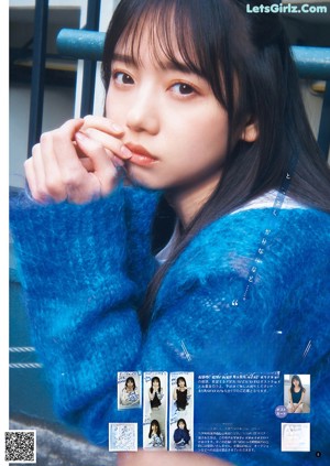 A young woman sitting on a chair wearing a blue cardigan.