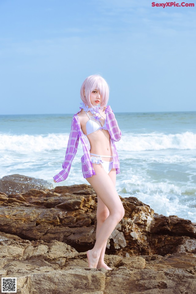 A woman in a bikini standing on a rock by the ocean.