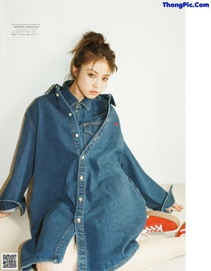 A woman sitting on the floor wearing a denim jacket and jeans.
